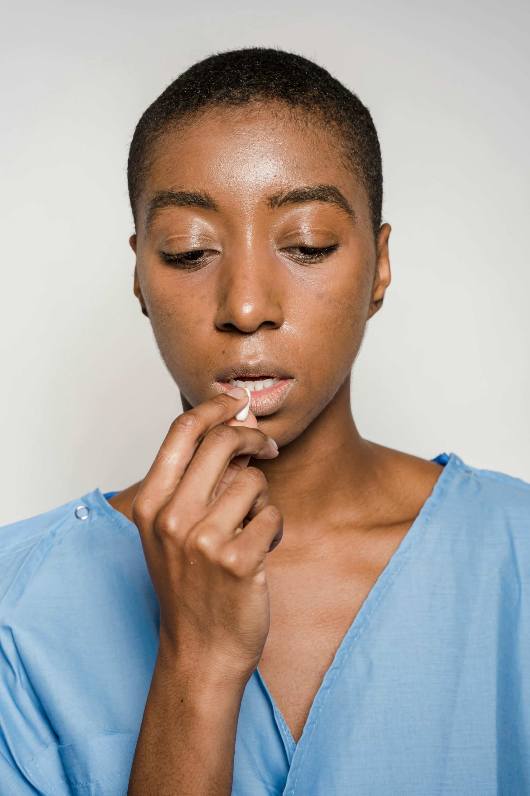 African American woman in blue robe taking medication on white background.